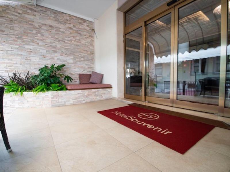 Taras hotelowy z miejscem do siedzenia, roślinami i czerwonym dywanikiem przy szklanych drzwiach przesuwnych.