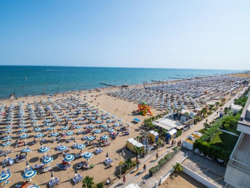 Widok na zatłoczoną piaszczystą plażę z licznymi parasolami i leżakami nad morzem.