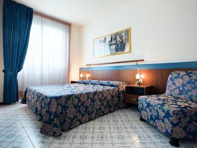 Hotelkamer met tweepersoonsbed, blauw patroon gordijnen en bank, helder daglicht