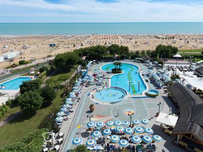 Grand bassin d'hôtel avec parasols, transats et vue sur la plage et la mer en arrière-plan.