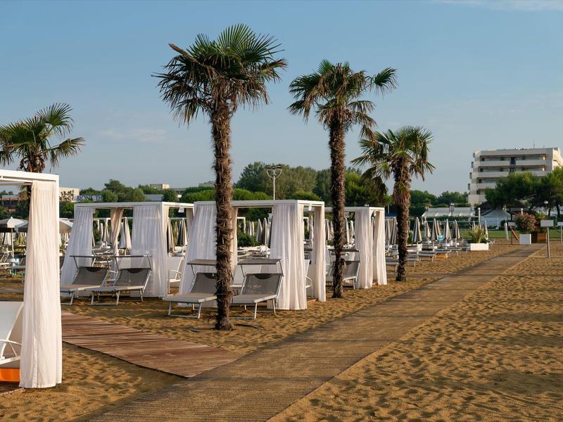 Strand met palmbomen, witte gordijnen en ligstoelen voor hotelgebouwen onder een heldere hemel