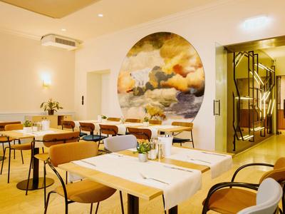 Restaurant mit modernem Interieur, gedeckten Tischen und rundem Wandbild in warmem Licht.