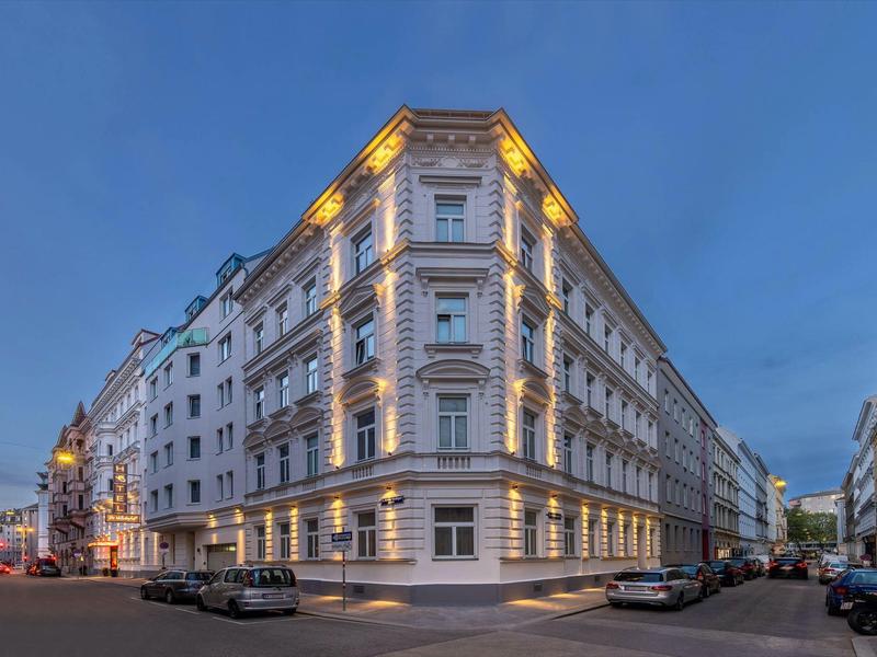 Klassisches Eckgebäude mit weißer Fassade und symmetrischen Fenstern bei Abenddämmerung.