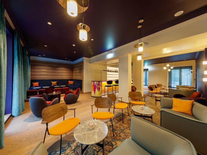 Modern eingerichteter Aufenthaltsraum mit bunter Beleuchtung, Sitzgruppen und Teppichboden.