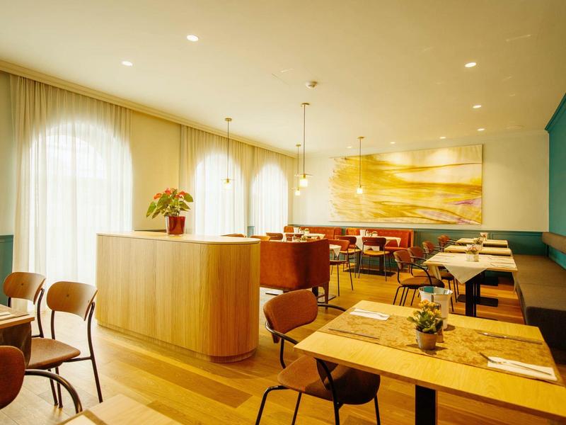 Modern eingerichtetes Restaurant mit Holztischen, Stühlen und warmem Licht sowie großen Fenstern.