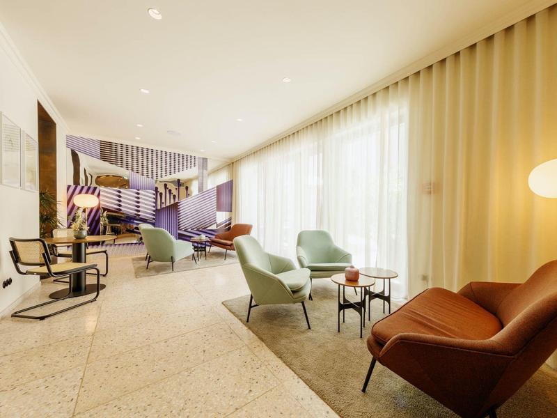 Hell eingerichteter, moderner Warteraum mit bequemen Sesseln und großen Fenstern mit Vorhängen.