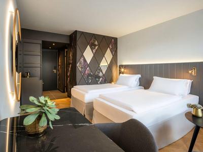 Modern eingerichtetes Hotelzimmer mit zwei Einzelbetten, geometrischer Wandgestaltung und Pflanzen.