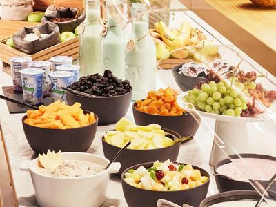 Buffet mit verschiedenen Schalen und Tellern, gefüllt mit Obst, Snacks, Joghurt und Milchflaschen.