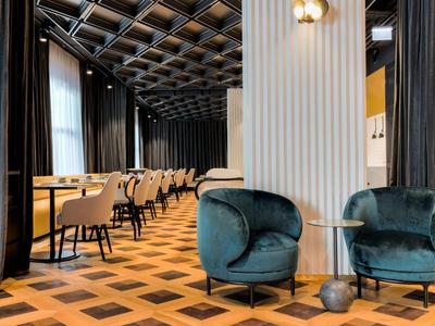 Eleganter Gastraum mit dunkelgrünen Sesseln, schwarzen Gardinen und Parkettboden mit geometrischem Muster.