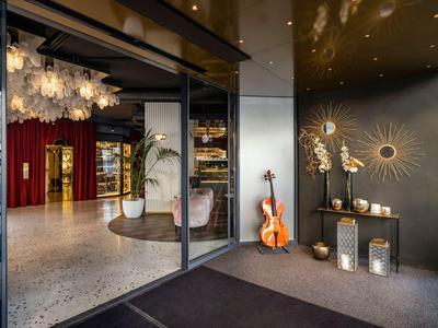 Moderner Hoteleingang mit Glas, dunkler Einrichtung und dekorativen Akzenten wie Geigen und Sonnenwandbildern.