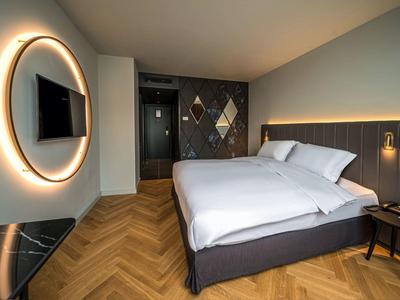 Modernes Hotelzimmer mit Doppelbett, Holzboden, großem runden Spiegel und LED-Beleuchtung.