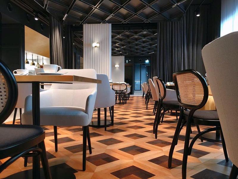 Moderner Restaurantbereich mit gemustertem Holzboden und gemischten weißen und schwarzen Stühlen.