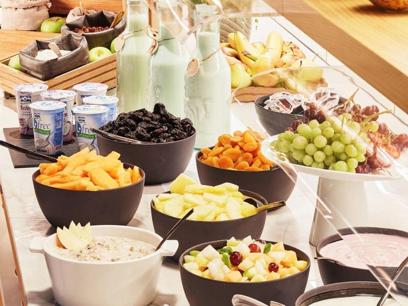 Buffet mit verschiedenen Schalen und Tellern, gefüllt mit Obst, Snacks, Joghurt und Milchflaschen.