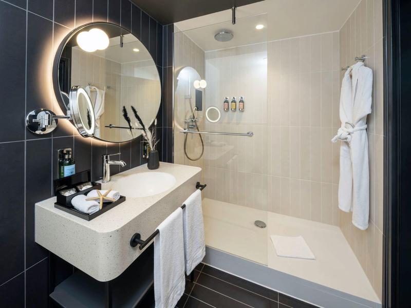 Modernes Badezimmer mit großer Dusche, rundem beleuchtetem Spiegel und weißem Waschbecken.