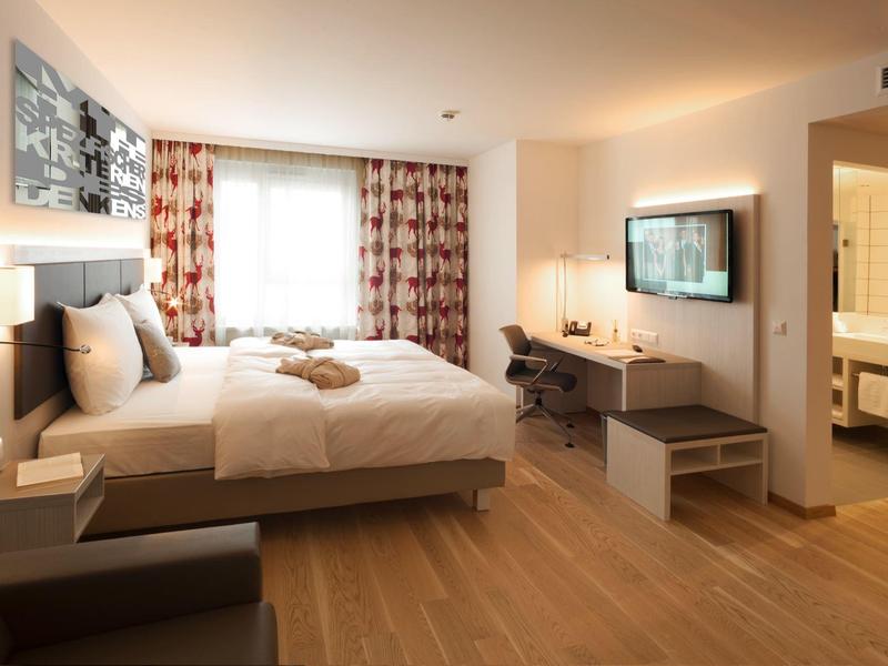 Modern eingerichtetes Hotelzimmer mit Doppelbett, Schreibtisch und Fernseher.