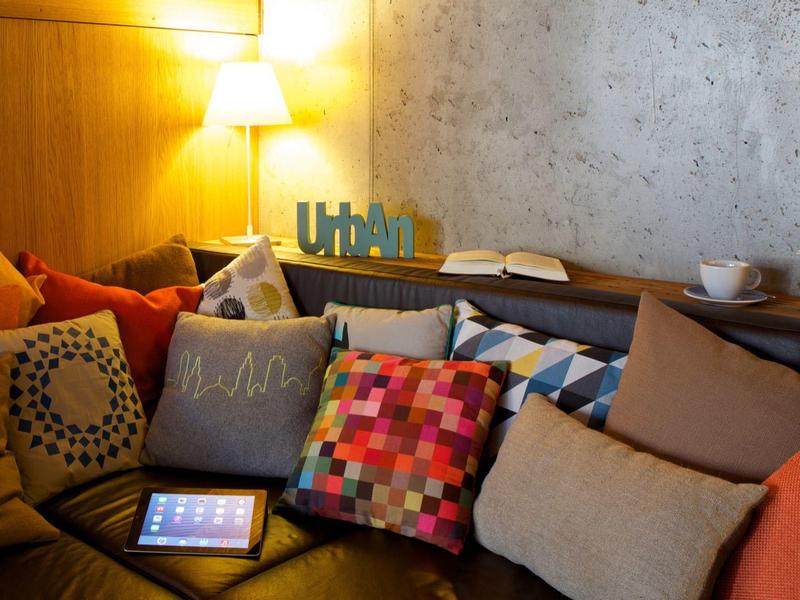 Gemütliche Sitzecke mit bunten Kissen, Tablet und einer hellen Lampe an der Wand.