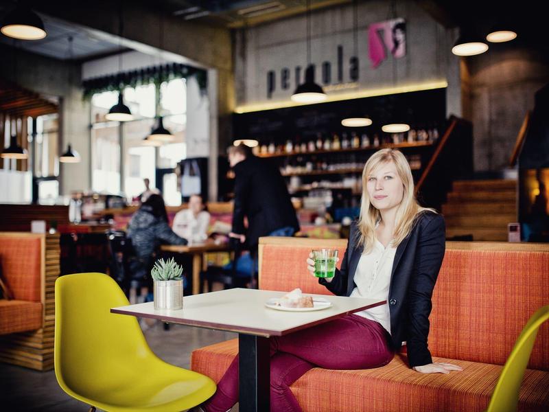 Frau sitzt entspannt in modernem Café mit orangenen Sitzbänken und gelben Stühlen.