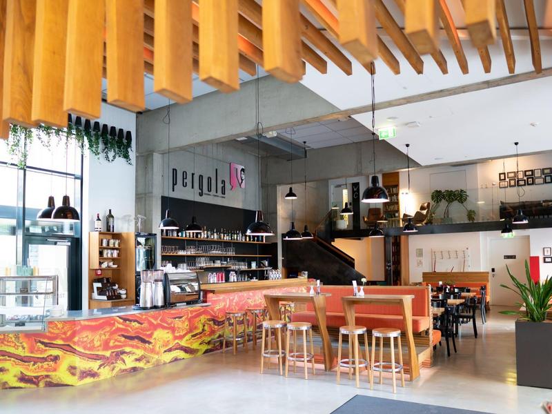 Modernes Café mit hölzernen Deckenverkleidungen, langen Holztischen und gemütlicher Atmosphäre.