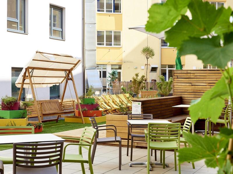 Moderner Innenhof mit grünen Stühlen, Tischgruppen, Holzbänken und einer Schaukel aus Holz.