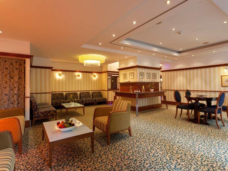 Gemütlicher Hotel-Loungebereich mit Teppichboden, Sesseln, Sofas, Tischen und Holzvertäfelungen.