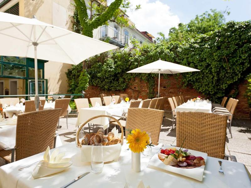 Terrassenrestaurant mit weißen Schirmen, geflochtenen Stühlen und gedeckten Tischen im Freien.