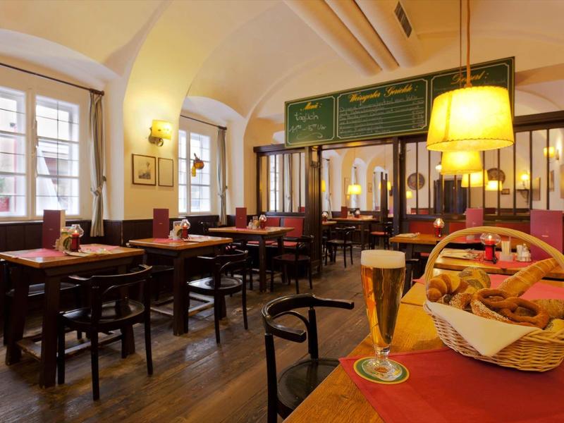 Gemütliches Café mit Holzmöbeln, großen Fenstern und warmem Licht, auf dem Tisch Brot und Bier.
