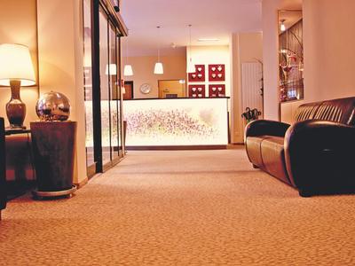 Hell beleuchteter Empfangsbereich mit Teppichboden, Lederstühlen und dekorativer Lampe.