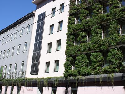 Mehrstöckiges Gebäude mit weißer Fassade und grünen Pflanzen an der rechten Seite.