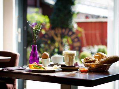 Gemütliches Frühstück mit Brötchen, Ei, Kaffee und Saft auf einem Tisch am Fenster.
