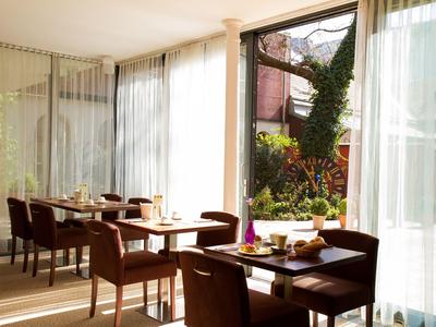 Hell eingerichteter Frühstücksraum mit Tischen und Sesseln, Blick auf grünen Garten.