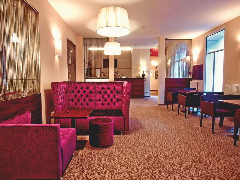 Moderne Hotel-Lounge mit roten Samtsofas, Teppichboden, Lampen und Holzvertäfelung.
