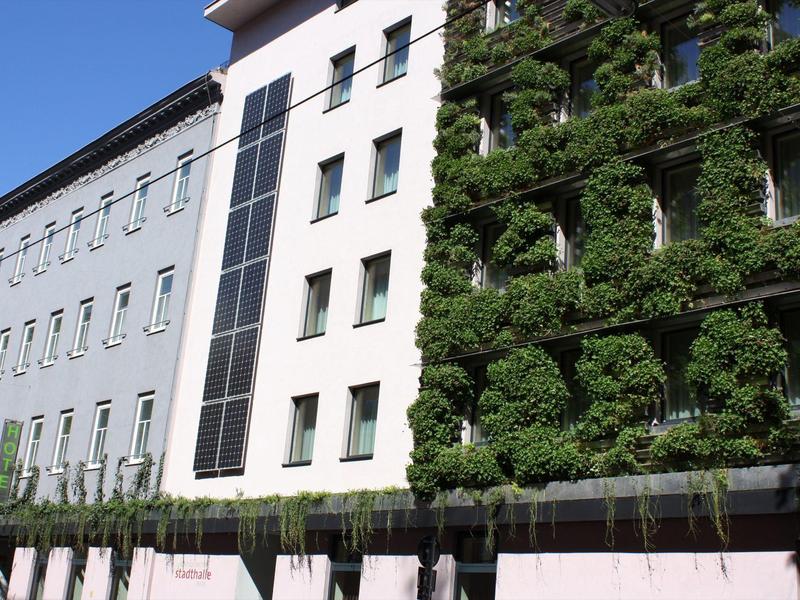 Mehrstöckiges Gebäude mit weißer Fassade und grünen Pflanzen an der rechten Seite.