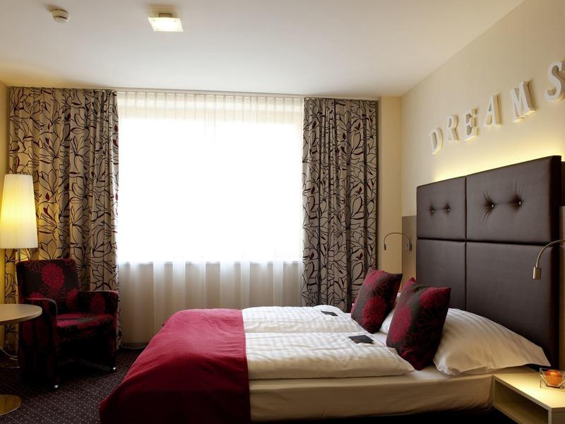 Ein einfach eingerichtetes Hotelzimmer mit zwei Betten, roter Bettwäsche und Vorhängen.