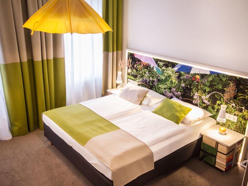 Modernes Schlafzimmer mit Doppelbett, grün-gelb-weißer Bettwäsche, Nachttischlampen und Vorhängen.