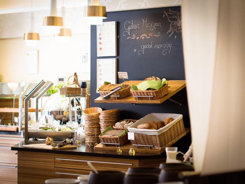 Gemütliches Café mit Brotkörben, Holzregal, schmiedeeisernem Gestell und warmem Licht.