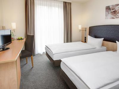 Modern eingerichtetes Hotelzimmer mit zwei Einzelbetten und Schreibtisch.