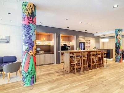 Moderne Hotel-Lounge mit farbenfrohen Säulen, Sitzgelegenheiten und Gemeinschaftstisch aus Holz.