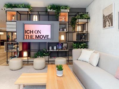 Modernes Wohnzimmer mit grauem Sofa, Holztisch, Pflanzen und Bücherregal im Hintergrund.