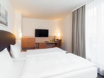 Modernes Hotelzimmer mit Doppelbett, großem Fernseher und Vorhängen an einem Fenster.