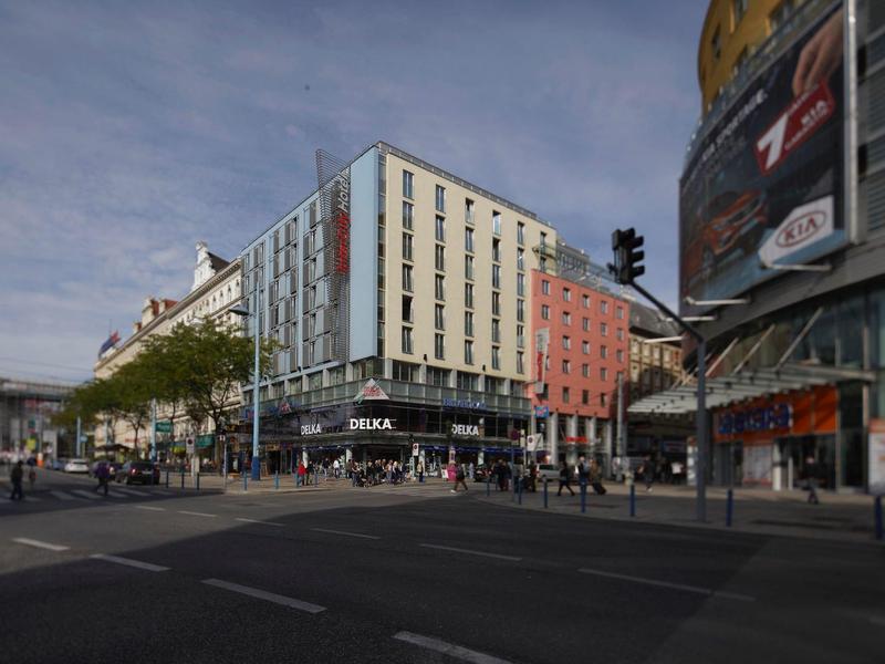 Städtische Kreuzung mit modernen Gebäuden, vorbei laufenden Fußgängern und Straßenschildern.