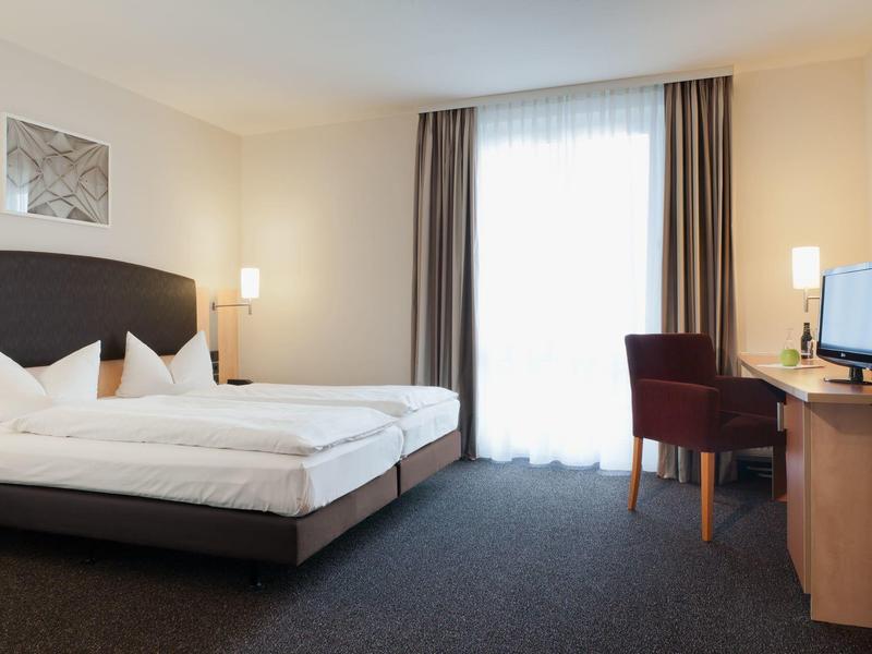 Helles Hotelzimmer mit Doppelbett, Schreibtisch, Stuhl und Fernseher.