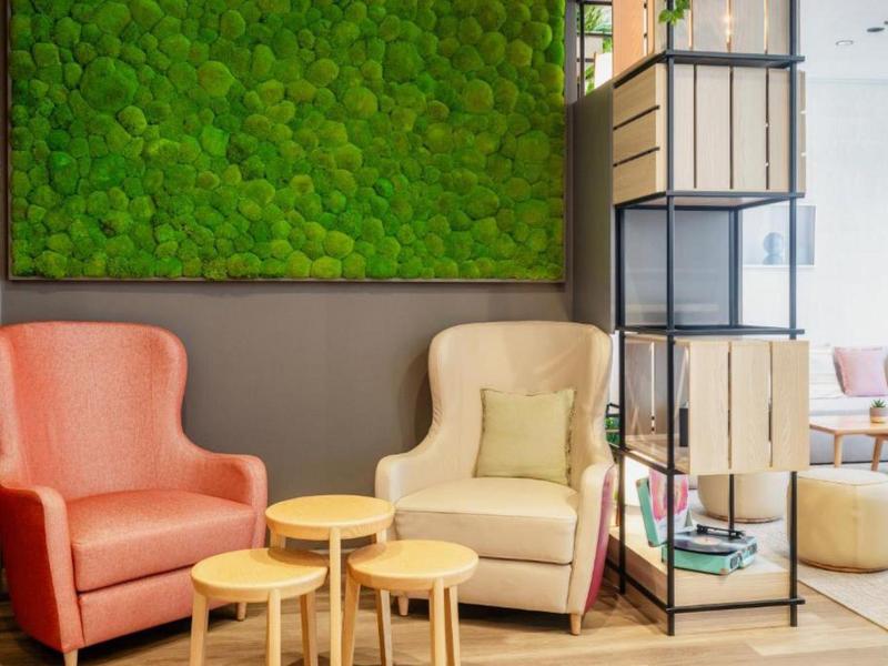 Gemütliche Sitzecke mit oranger und beige Sessel, grüner Wanddeko und runden Holztischen.