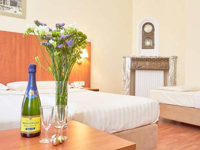 Hotelzimmer mit zwei Betten, Holzfußboden, Blumenstrauß, Sektflasche und Gläsern auf Tisch.