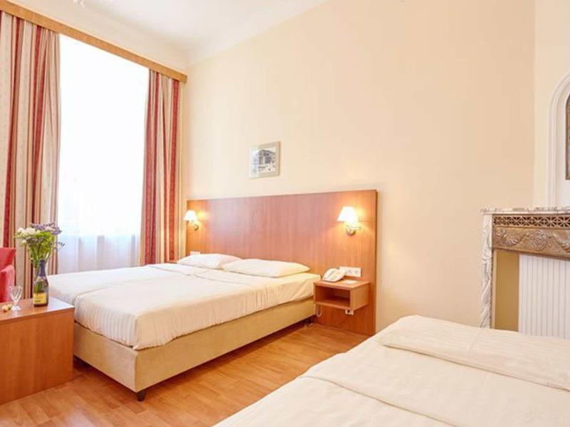 Helles Zweibettzimmer mit Holzfußboden, rotem Sessel, Wanduhr und Doppelbett.