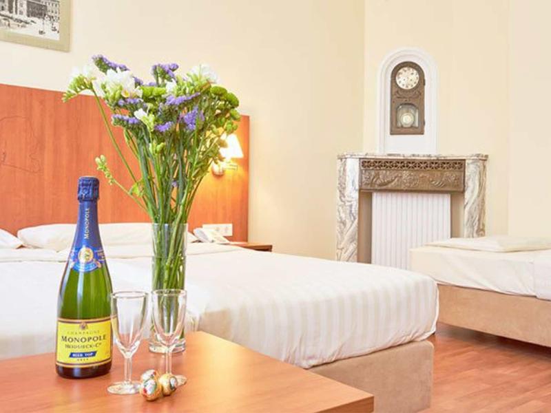 Hotelzimmer mit zwei Betten, Holzfußboden, Blumenstrauß, Sektflasche und Gläsern auf Tisch.
