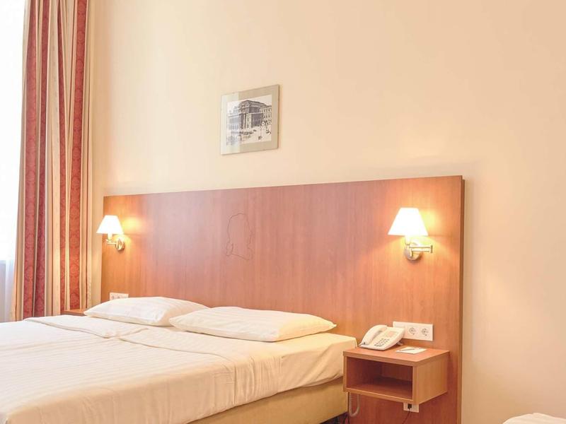 Helles Schlafzimmer mit Doppelbett, Holz-Kopfteil, zwei Wandlampen und Telefon auf Nachttisch.