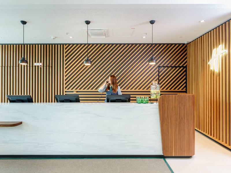 Moderne Hotellobby mit Holzvertäfelung und weißem Marmortresen, Mitarbeiter am Empfang.