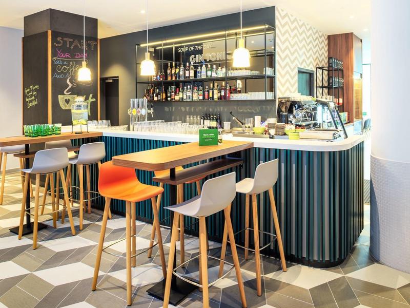 Moderner Hotelbarbereich mit farbigen Barhockern und geometrischem Bodenmuster.