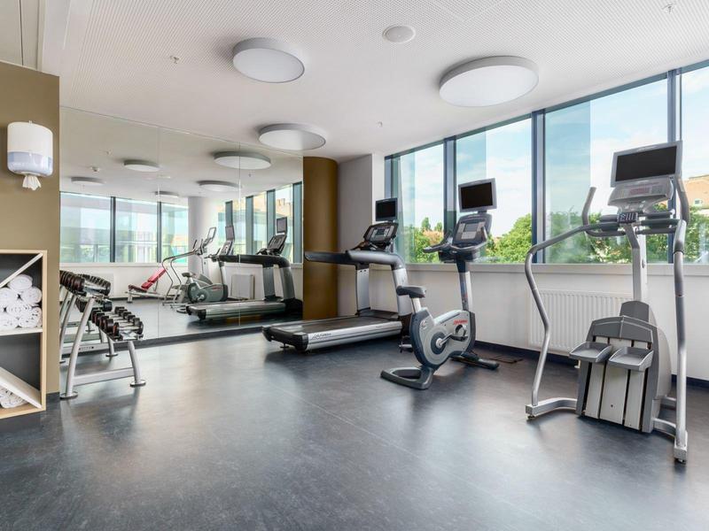 Moderner Fitnessraum mit Laufband, Fahrrädern und großem Spiegel neben breiten Fenstern.