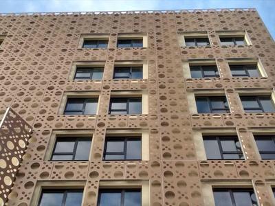 Fassade eines hohen Gebäudes mit geometrischem Lochmuster und mehreren Rechteckfenstern.